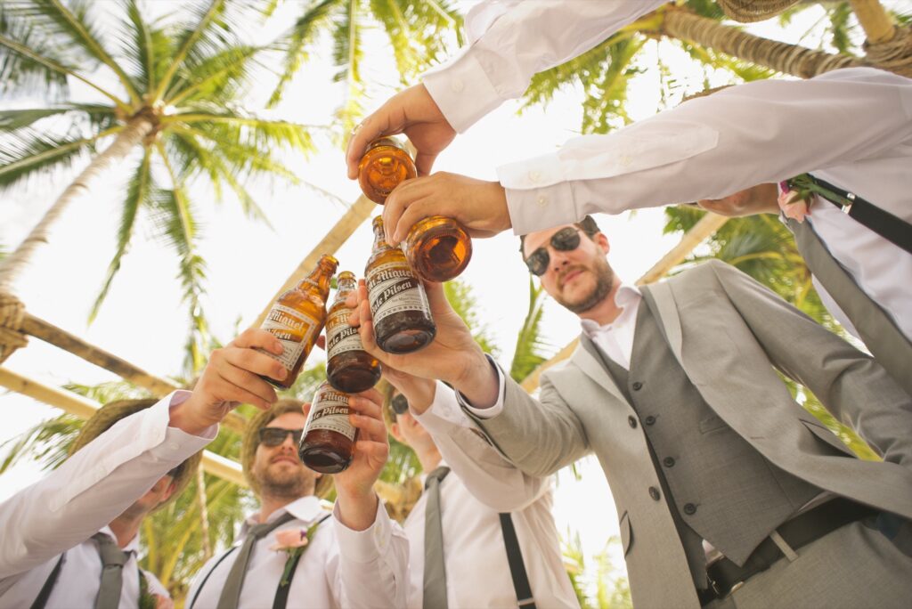 Friends in suits toasting beers on the beach