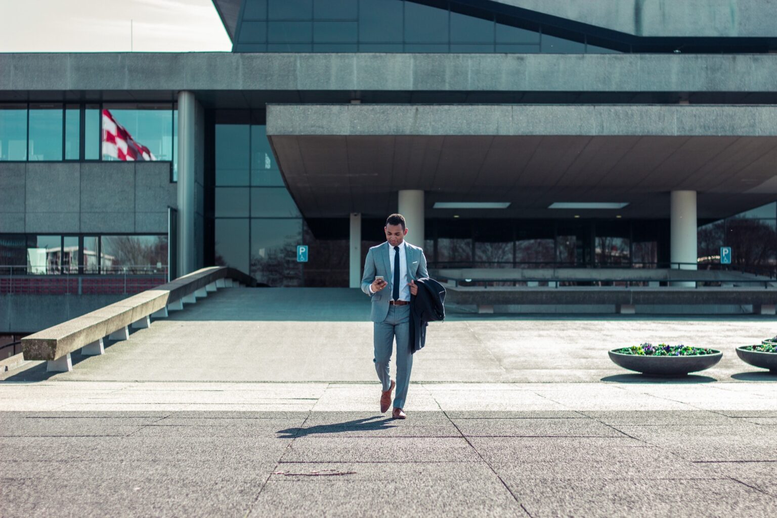 A man wearing a grey suit checks his phone while walking