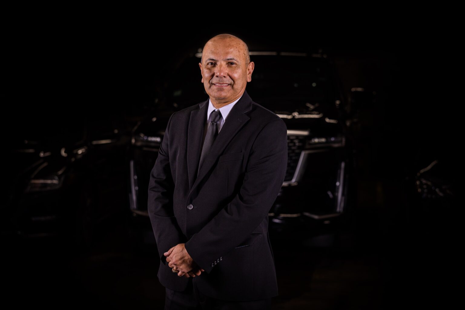 Magdiel Tapias standing proudly in front of luxury fleet cars
