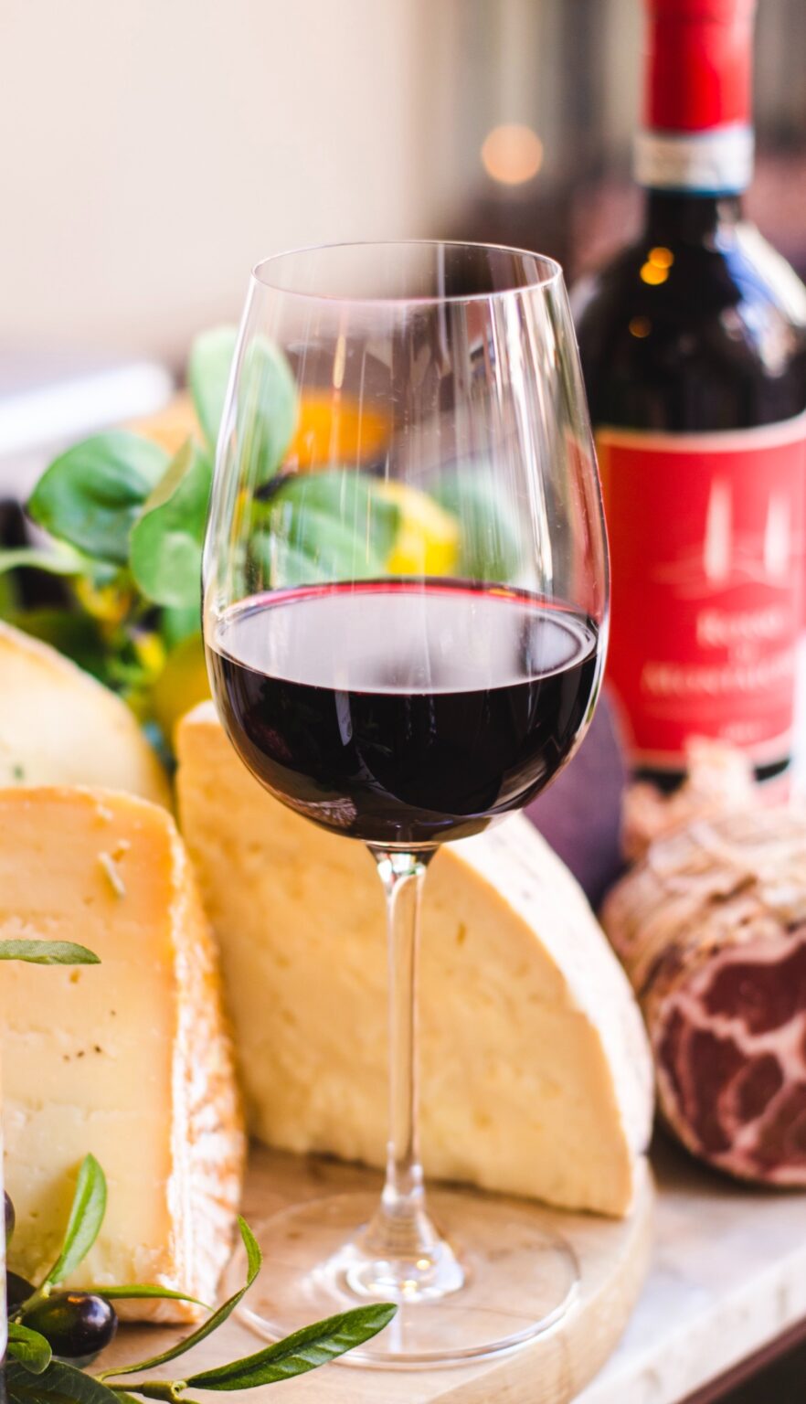 A glass of red wine on a meat and cheese tray