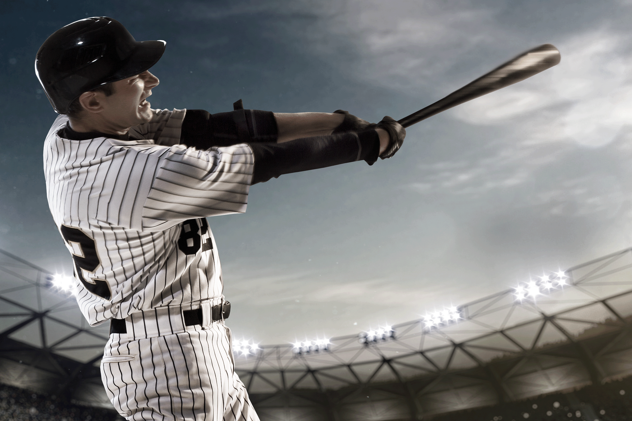 Baseball player swinging for the fences at dusk with the stadium lights shining in the background