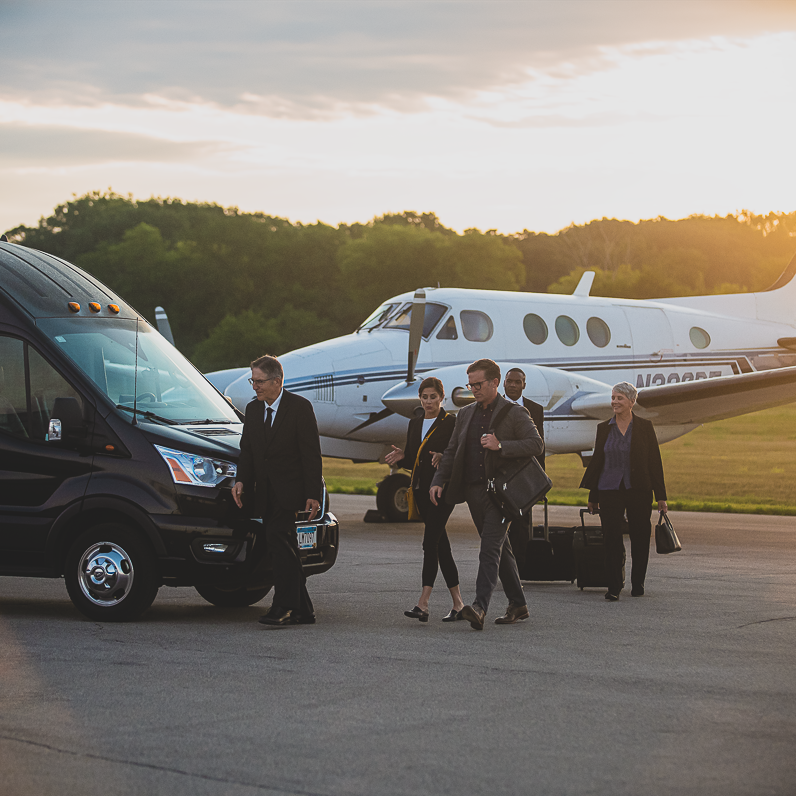 Chauffeur guiding business people onto corporate shuttle van for transportation to their final destination.