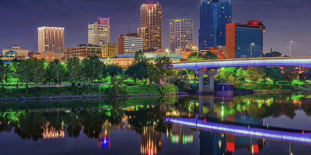 Skyline view of downtown Little Rock Arkansas at night, with vibrant reflections on the river.