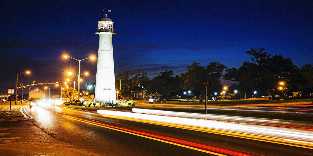 Biloxi lighthouse at night with traffic streaming around it.