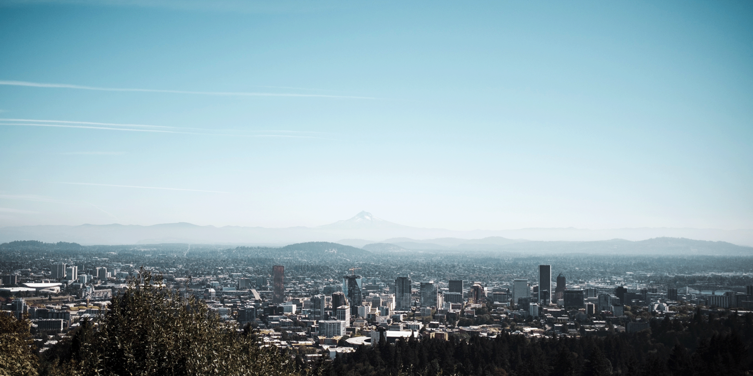 Aerial view of Portland Oregon showing the city expanding across the landscape with Mount Hood faded in the distance.