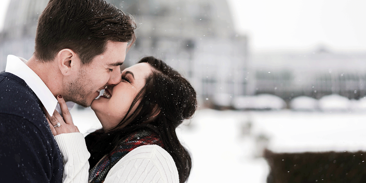 couple kissing in cozy winter wedding attire among the snow-covered grounds of their venue.